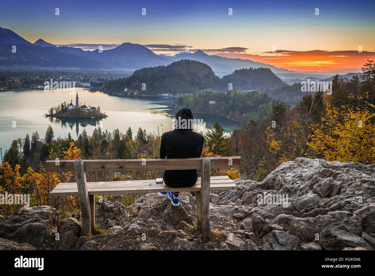 Bled, Slovenia - Runner woman relaxing and enjoying the beautiful autumn view and the colorful sunrise of Lake Bled sitting on a hilltop bench wearing Stock Photo