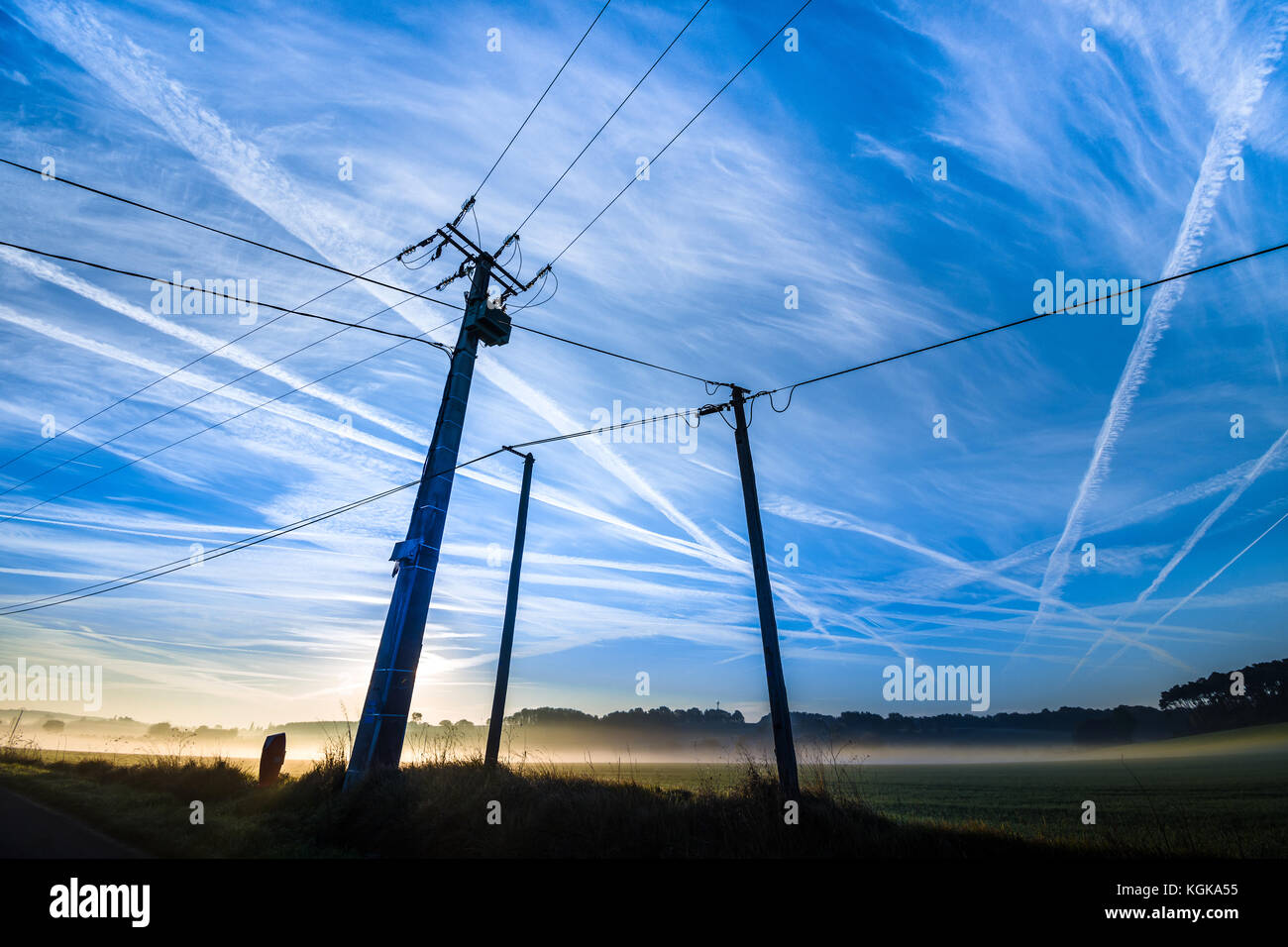 Electricity power lines and aircraft contrails - France. Stock Photo