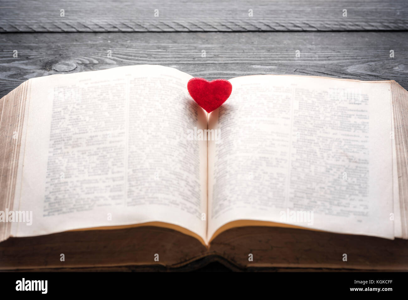 Education theme image with an antique open book with a red heart in the middle of it, on a vintage black table. A concept for love of learning, readin Stock Photo
