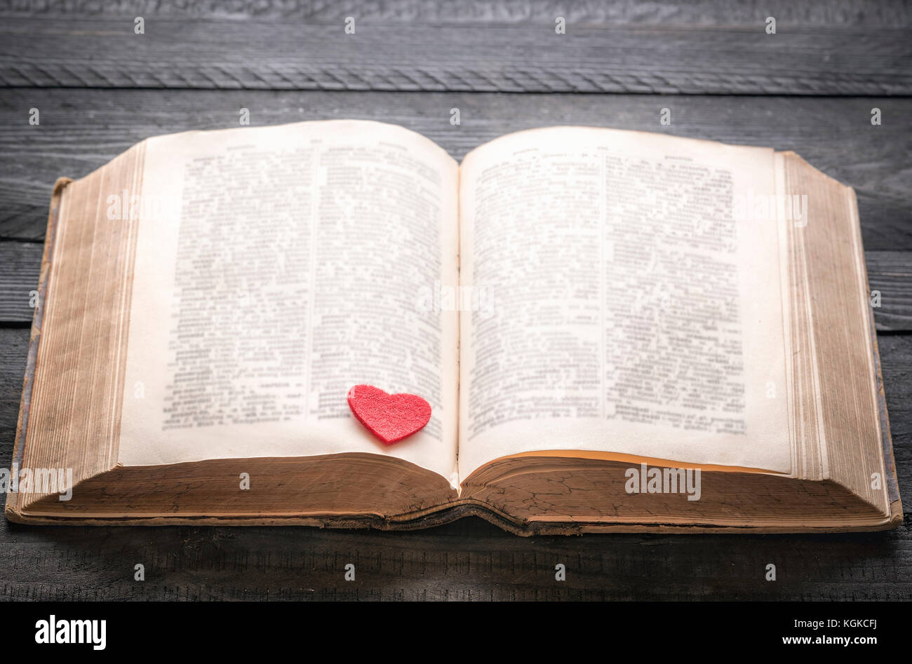 Open old book with a red little heart on its pages, displayed on a black wooden table. Concept for love of reading, education or romantic novel. Stock Photo