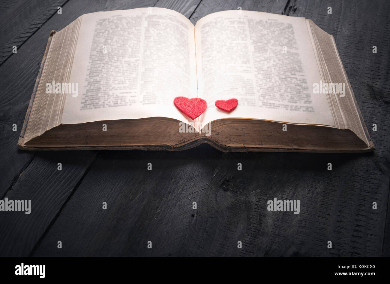 Antique open book with two red hearts on its pages, sitting on a black wooden background. A concept for the love of reading, learning, education or as Stock Photo