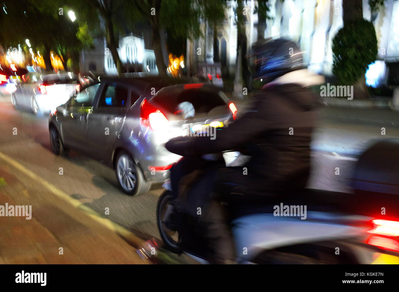 Moped rider passing between Kerb and moving cars in London, England
