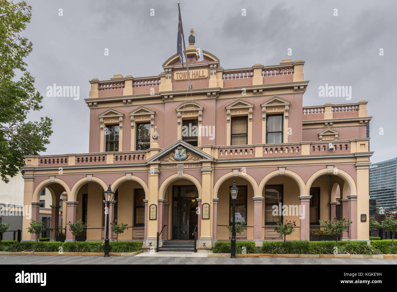 Parramatta, Australia - March 24, 2017: Brown historic Town Hall building under heavy rainy sky. Lanterns and green vegetation around. Stock Photo