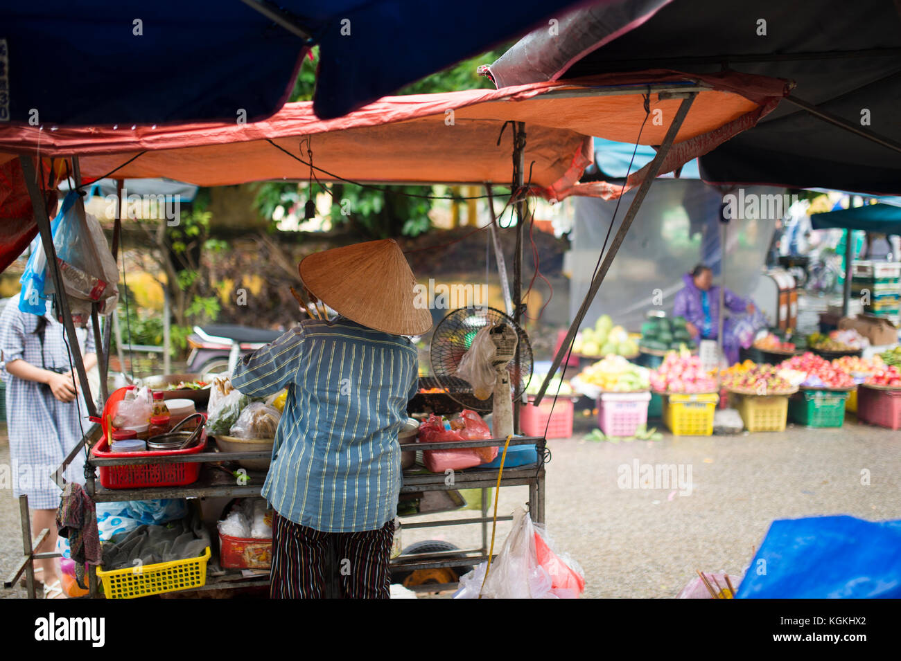 -Selective focus- Unidentified woman with typical vietnamese conical hats sell fresh vegetables and meat skewers on a street market in Hoi An, Vietnam Stock Photo