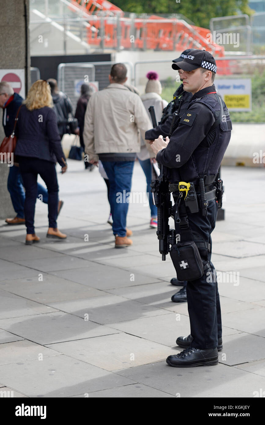 Armed police in London watching over passing public outside Tower Hill railway station. Stock Photo