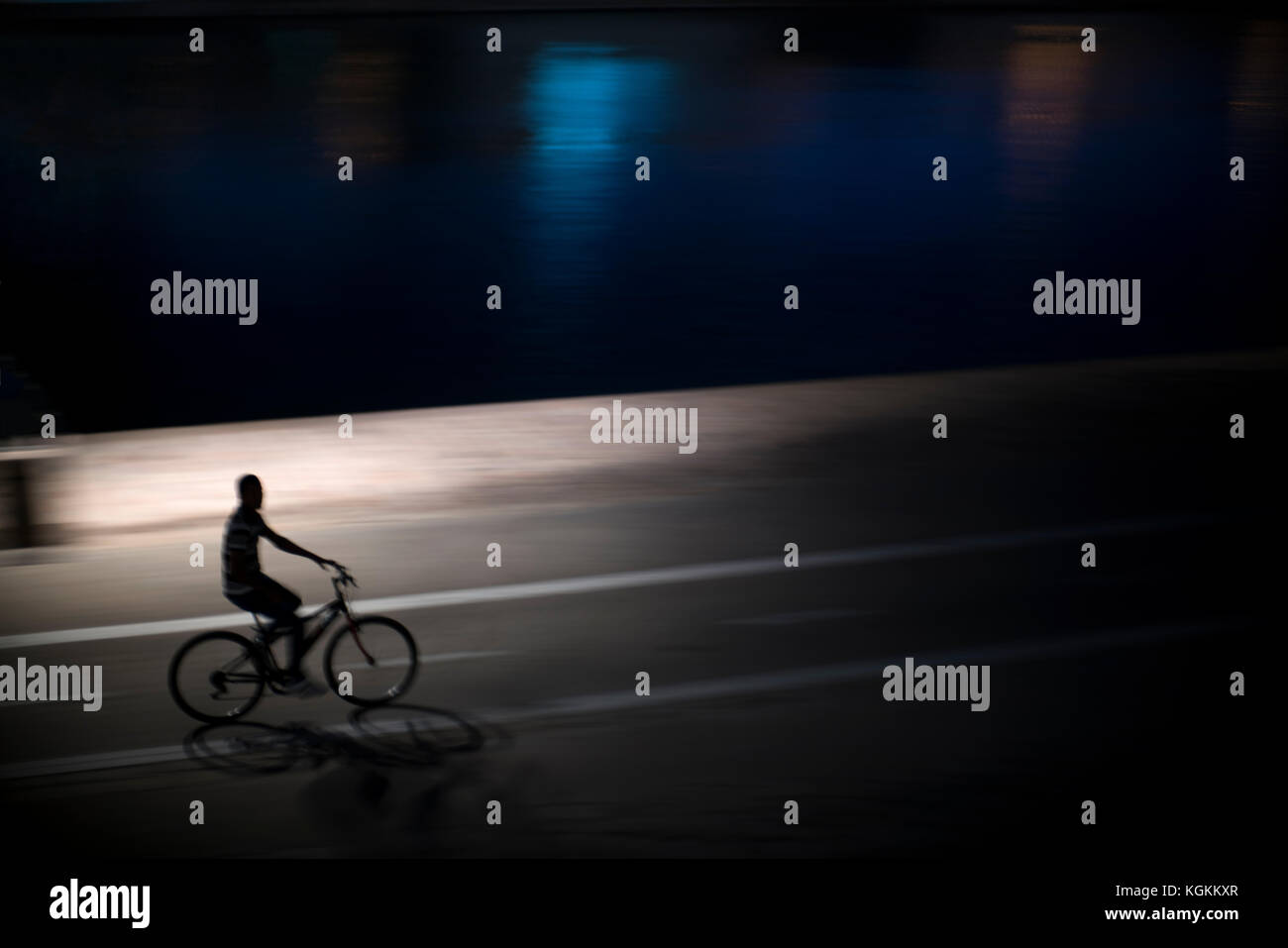 Cyclist riding by the Guadalquivir river at night, Seville, Spain Stock Photo