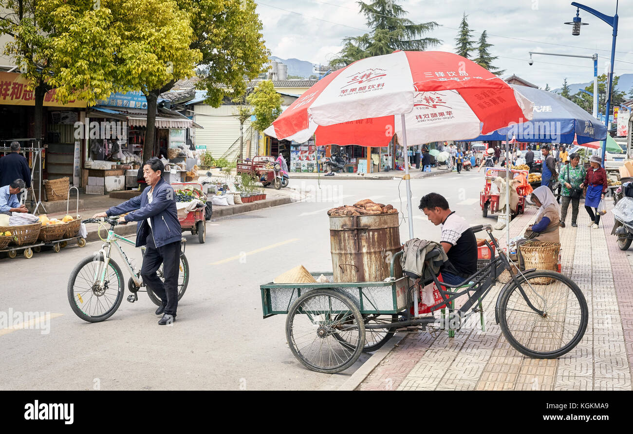 Lijiang, Yunnan, China - September 28, 2017: Food vendor waits for customers with a bicycle stall on a street of Lijiang. Stock Photo