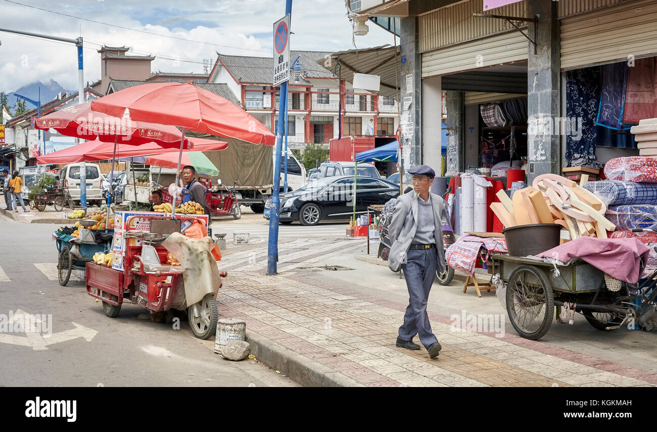 Lijiang, Yunnan, China - September 28, 2017: Pedestrian passes a food vendor with bicycle stall on a street of Lijiang. Stock Photo