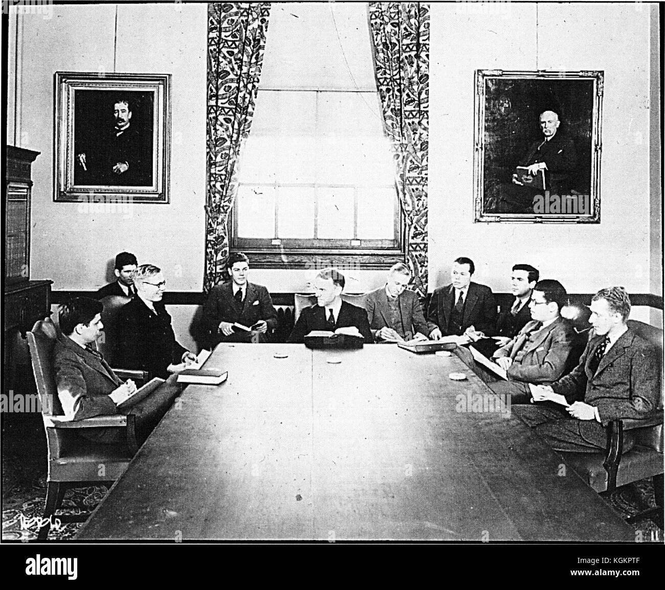 A history class at the Johns Hopkins University in Baltimore, Maryland; eleven men sitting around wooden table; portraits of JM Vincent and HB Adams hanging on wall, 1920. Stock Photo