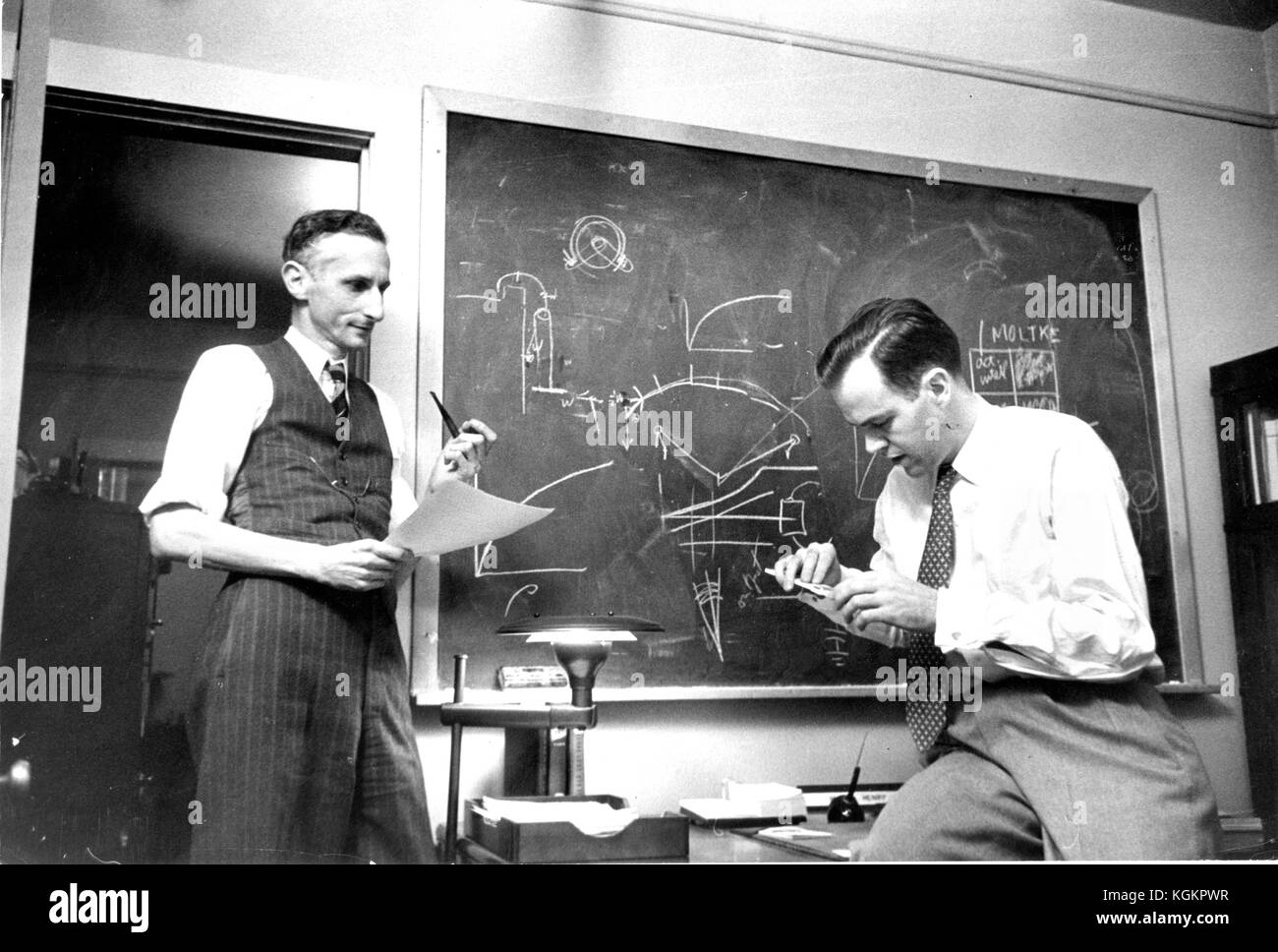 Candid of two men in a Johns Hopkins University classroom in front of a blackboard covered in mathematical equations, including James Herbert Henry, staff member at Johns Hopkins University, at 40 years old, and Macon Fry, operations analyst at the Operations Research Office at Johns Hopkins University, at 45 years old, Baltimore, Maryland, 1952. () Stock Photo