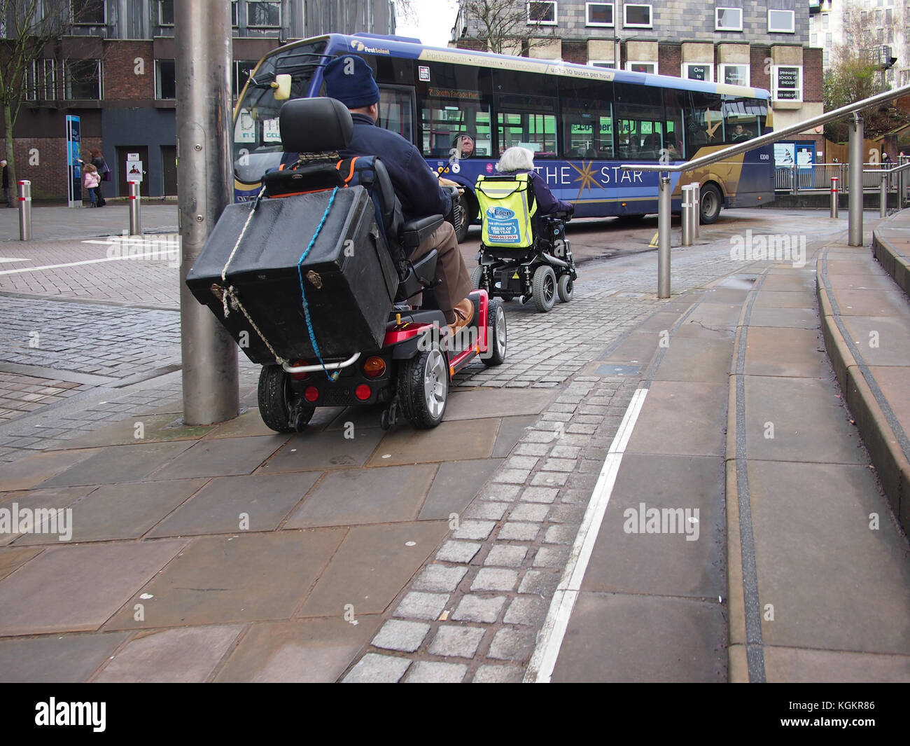 Two senior adults drive mobility scooters on a city centre pavement