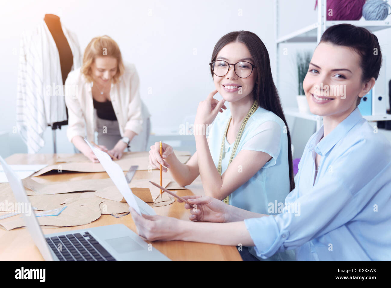 Smiling cute tailors sitting at the table and working Stock Photo - Alamy