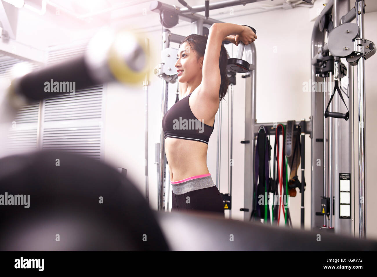 young asian woman working out in gym using dumbbell. Stock Photo