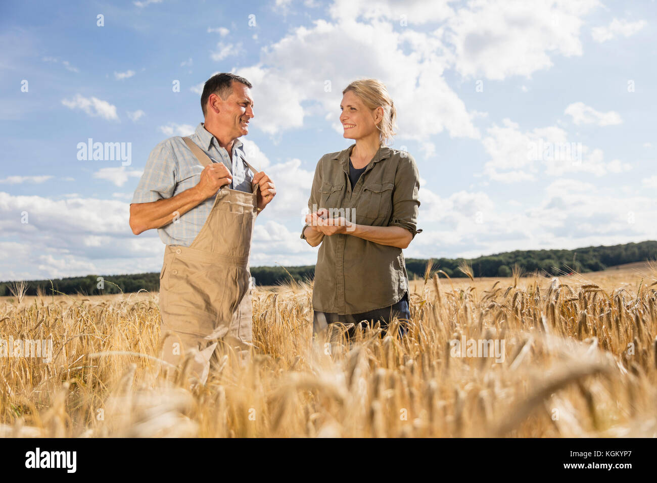 Happy mature couple talking while standing amidst crops at farm against sky Stock Photo