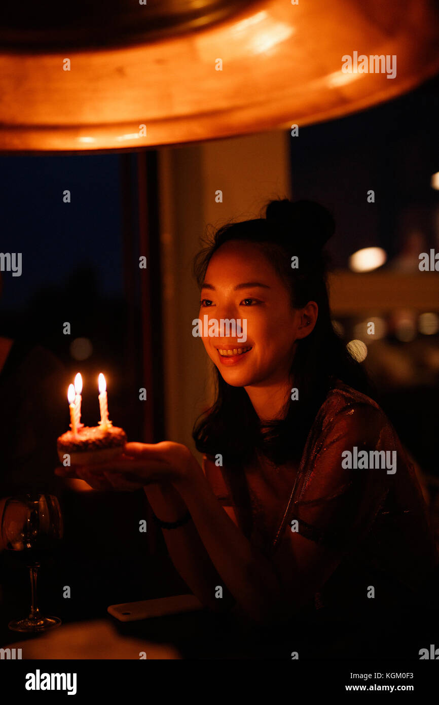 Happy woman holding small birthday cake with candles in darkroom Stock Photo