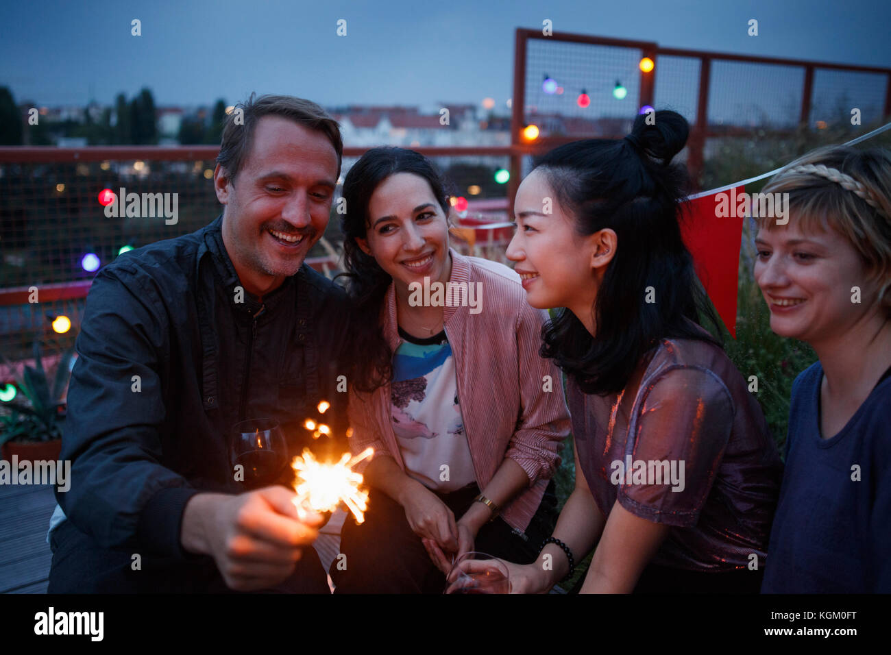 Happy man holding sparkler while sitting with female friends at night Stock Photo