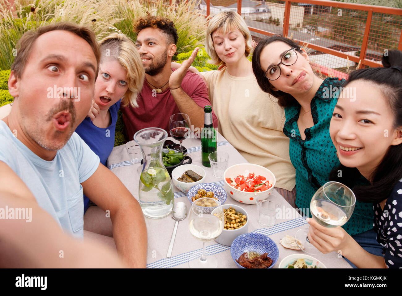 Portrait of playful friends making faces while sitting at outdoor table at patio Stock Photo