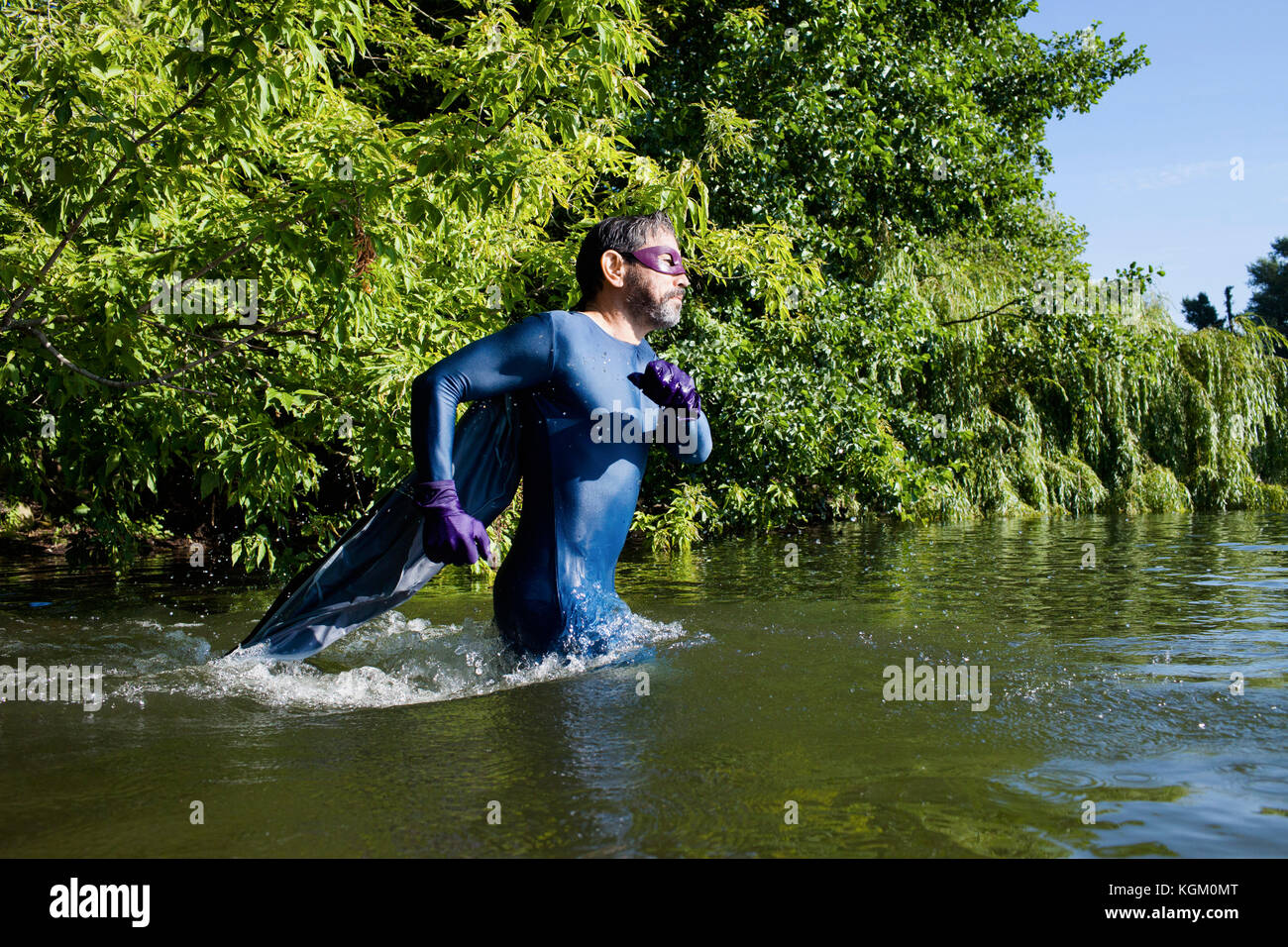 Side view of mature superhero running in river against trees Stock Photo
