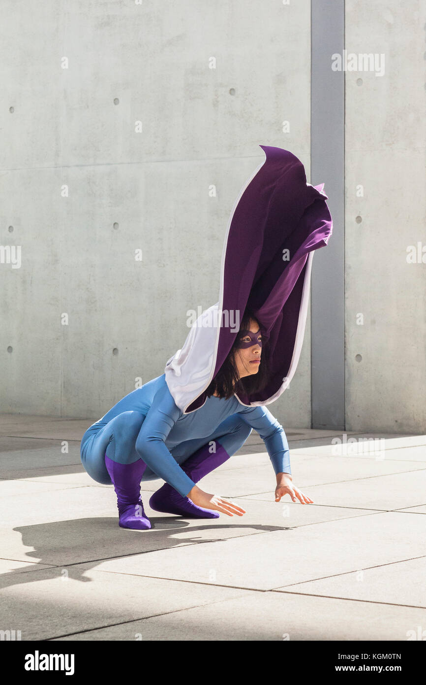 Female superhero wearing purple cape crouching on floor by wall Stock