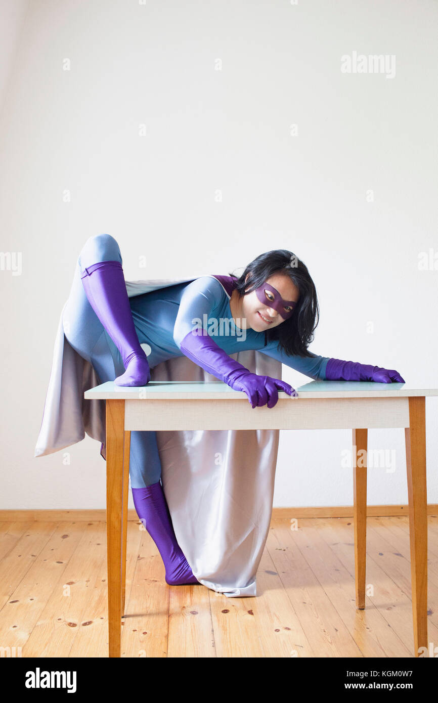 Young female superhero climbing on table against white wall Stock Photo