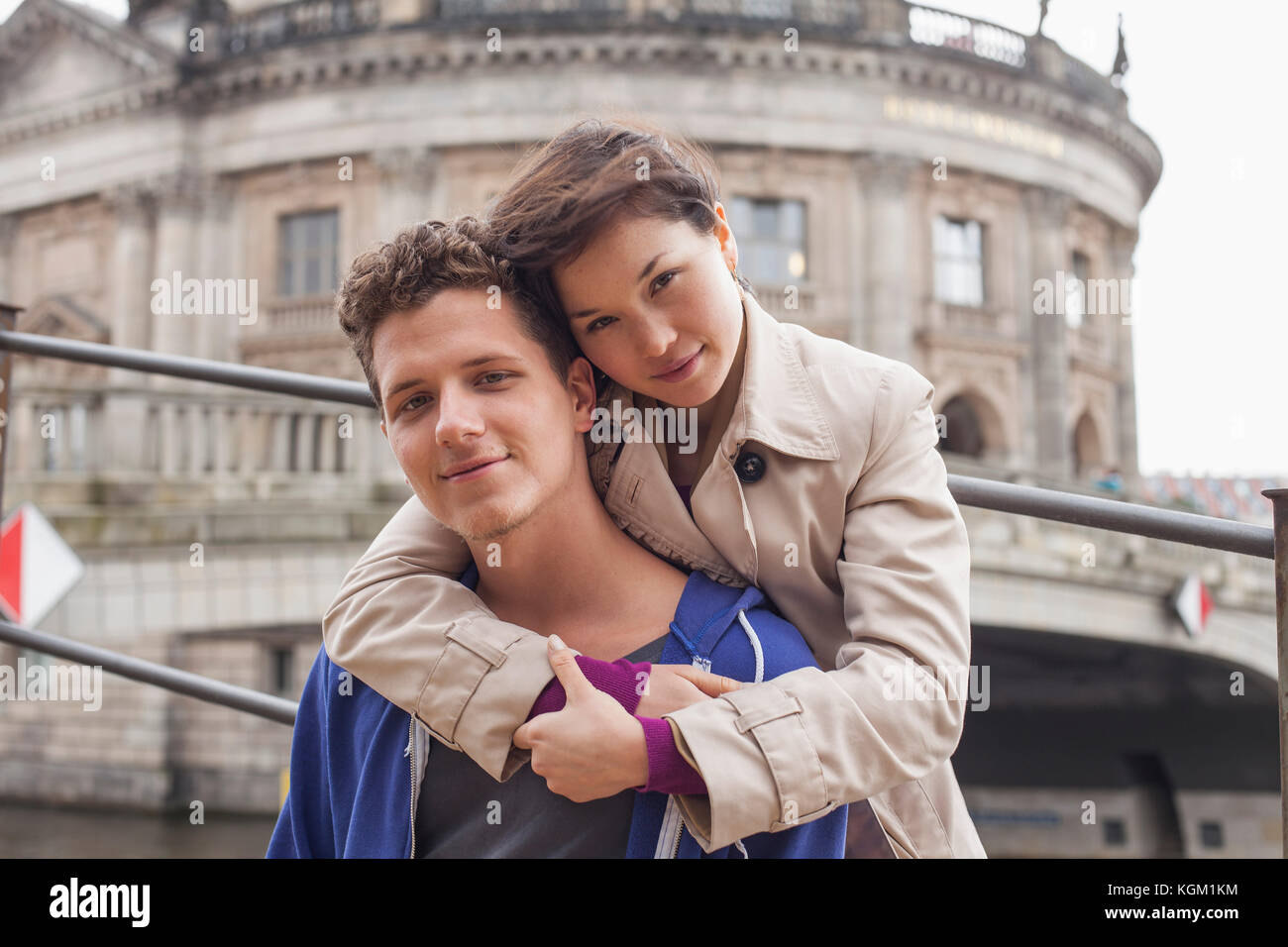 Low angle portrait of woman embracing male friend against Bode Museum, Berlin, Germany Stock Photo
