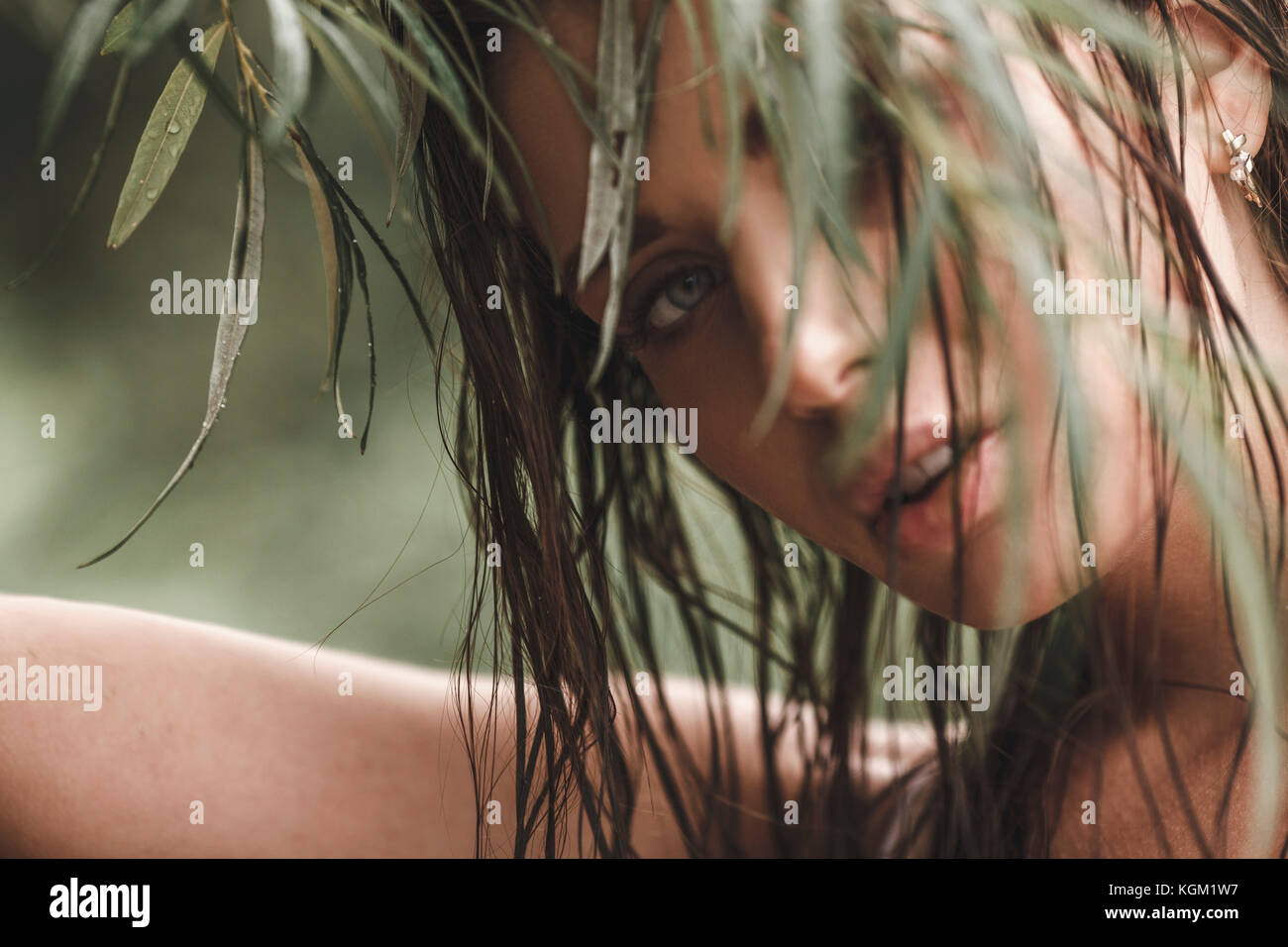 Close-up portrait of young woman with wet hair looking through leaves Stock Photo