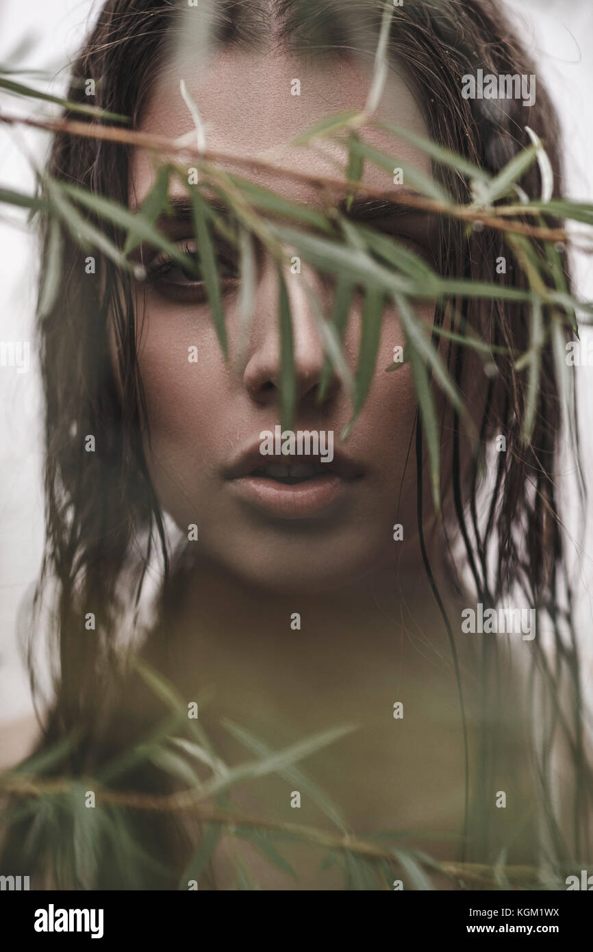 Close-up portrait of woman with wet hair looking through branches Stock Photo