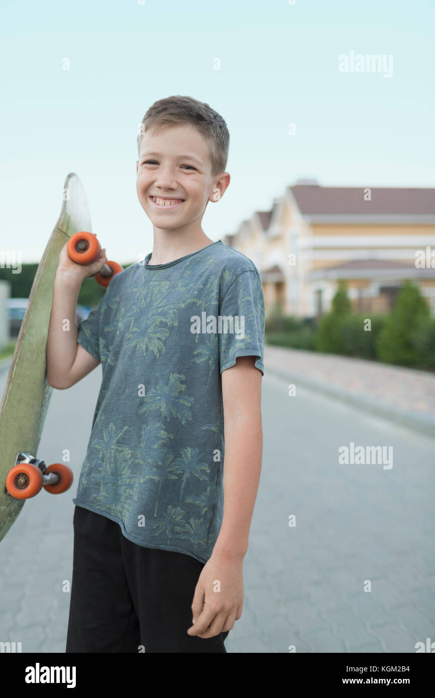 Portrait of smiling boy holding skateboard while standing on street Stock Photo