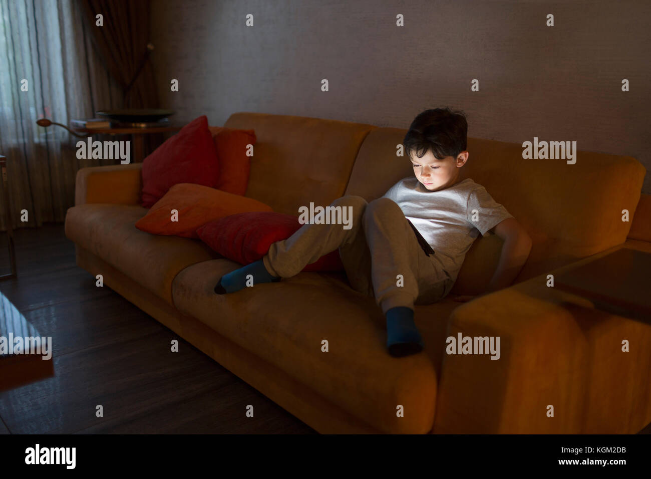 Full length of boy using digital tablet while sitting on sofa at home ...