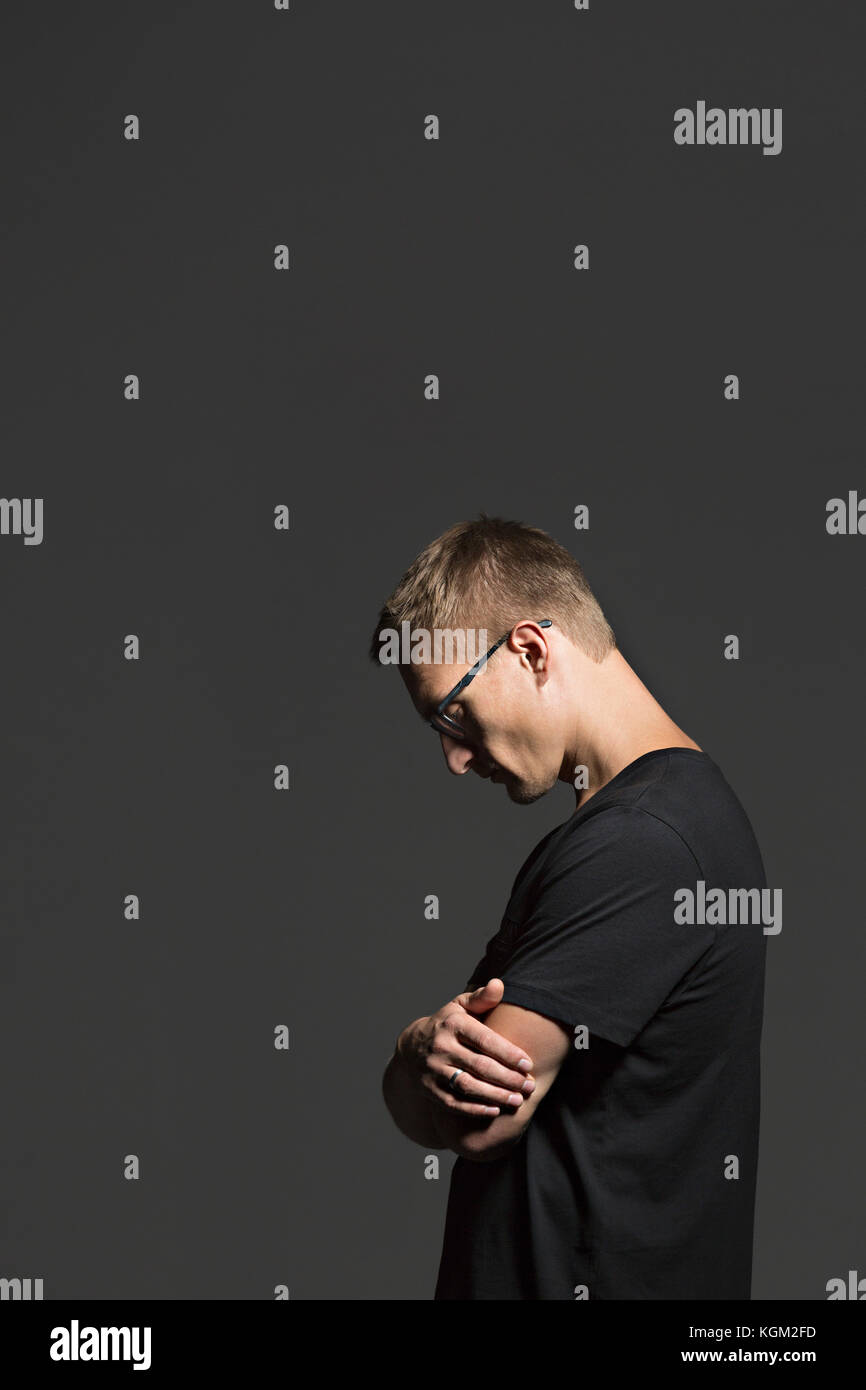 Side view of mid adult man standing with arms crossed against gray background Stock Photo