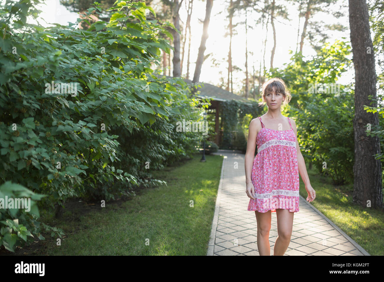 Woman wearing pink dress walking on pathway amidst plants in yard Stock Photo