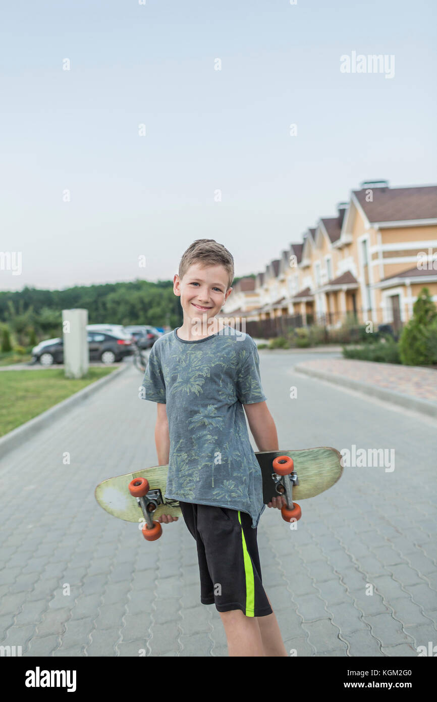 Portrait of smiling boy holding skateboard while standing on street against clear sky Stock Photo