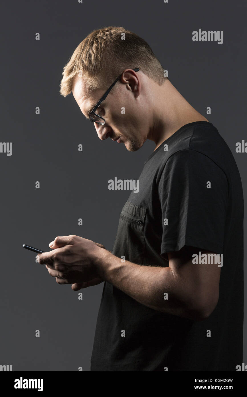 Side view of man using mobile phone while standing against gray background Stock Photo
