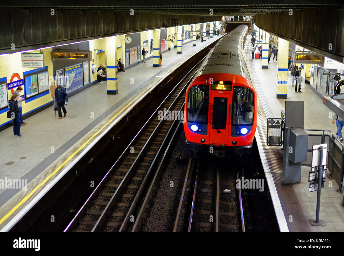 An underground train at the platform of Aldgate East station on the London Underground system with commuters waiting Stock Photo