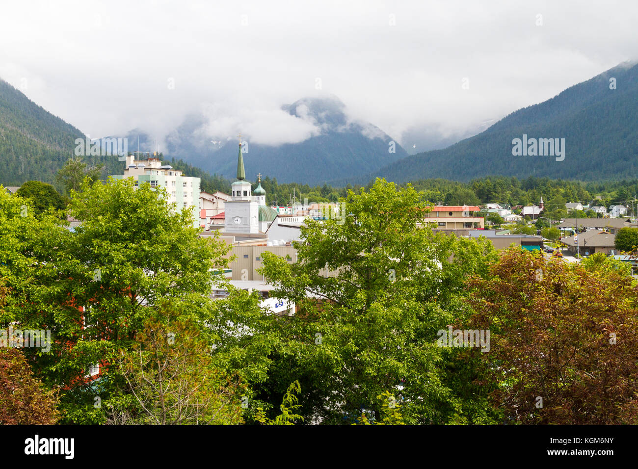 An elevated view of Sitka, Alaska seen through trees with mountains and