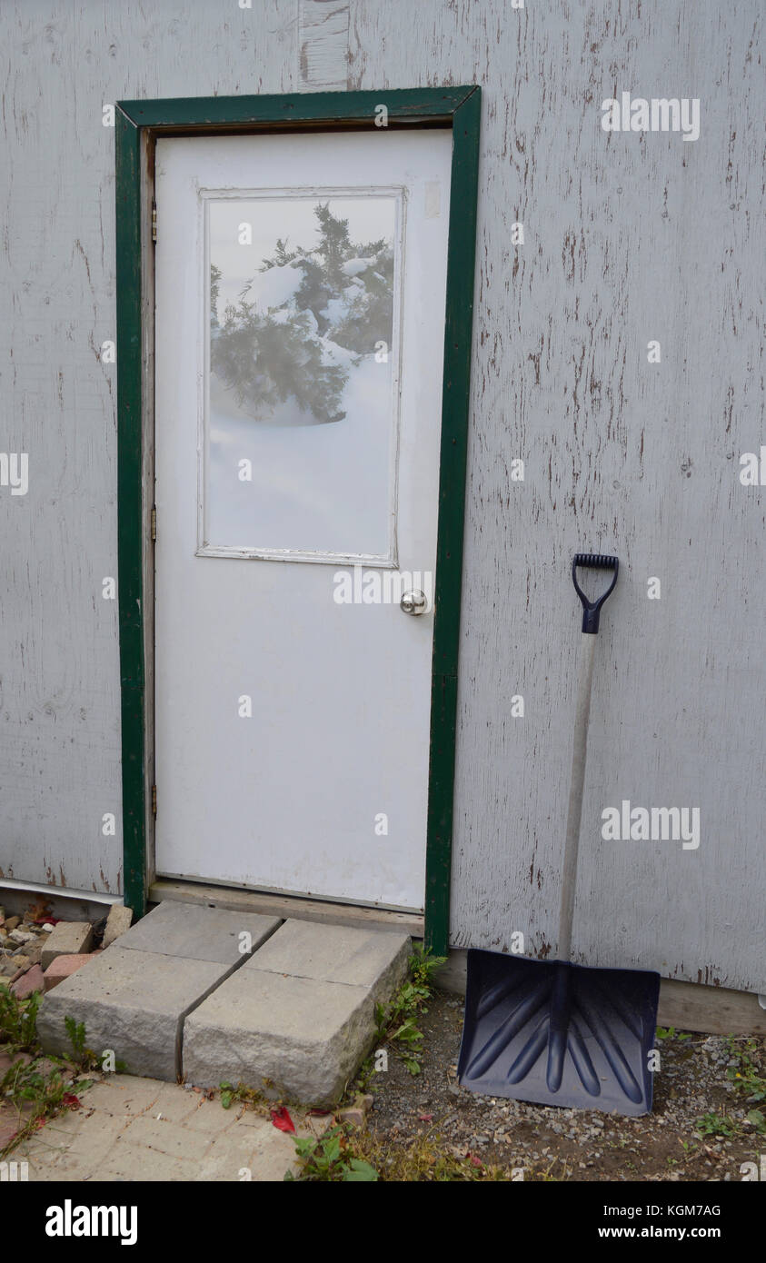 picture of an old shed with a snow shovel leaning on the wall - getting ready for bad weather and winter snow Stock Photo