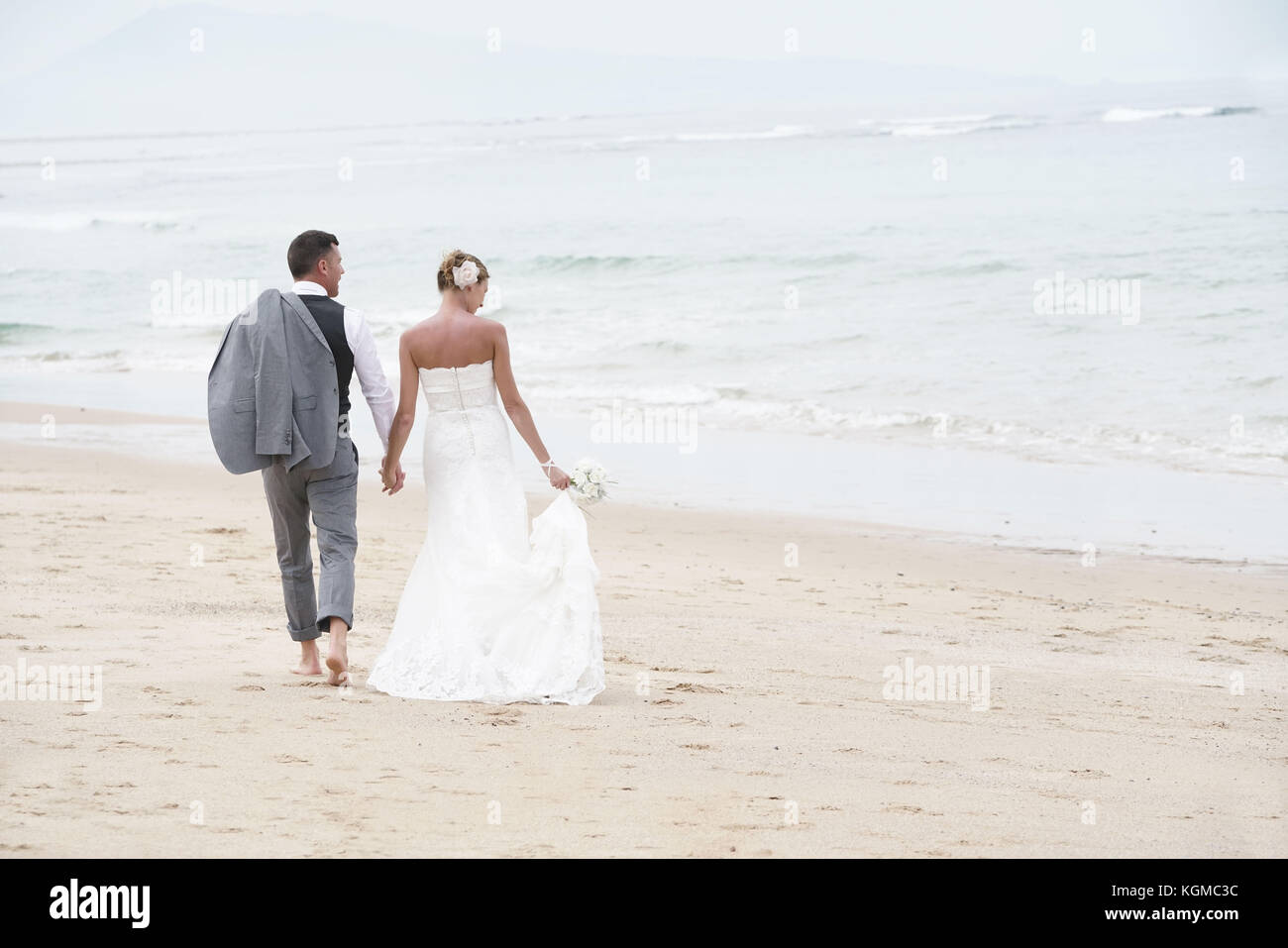 Back View Of Bride And Groom Walking On The Beach Stock Photo