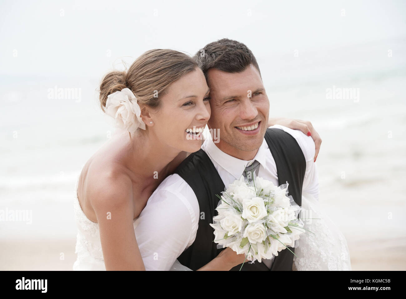 Groom giving piggyback ride to bride on the beach Stock Photo