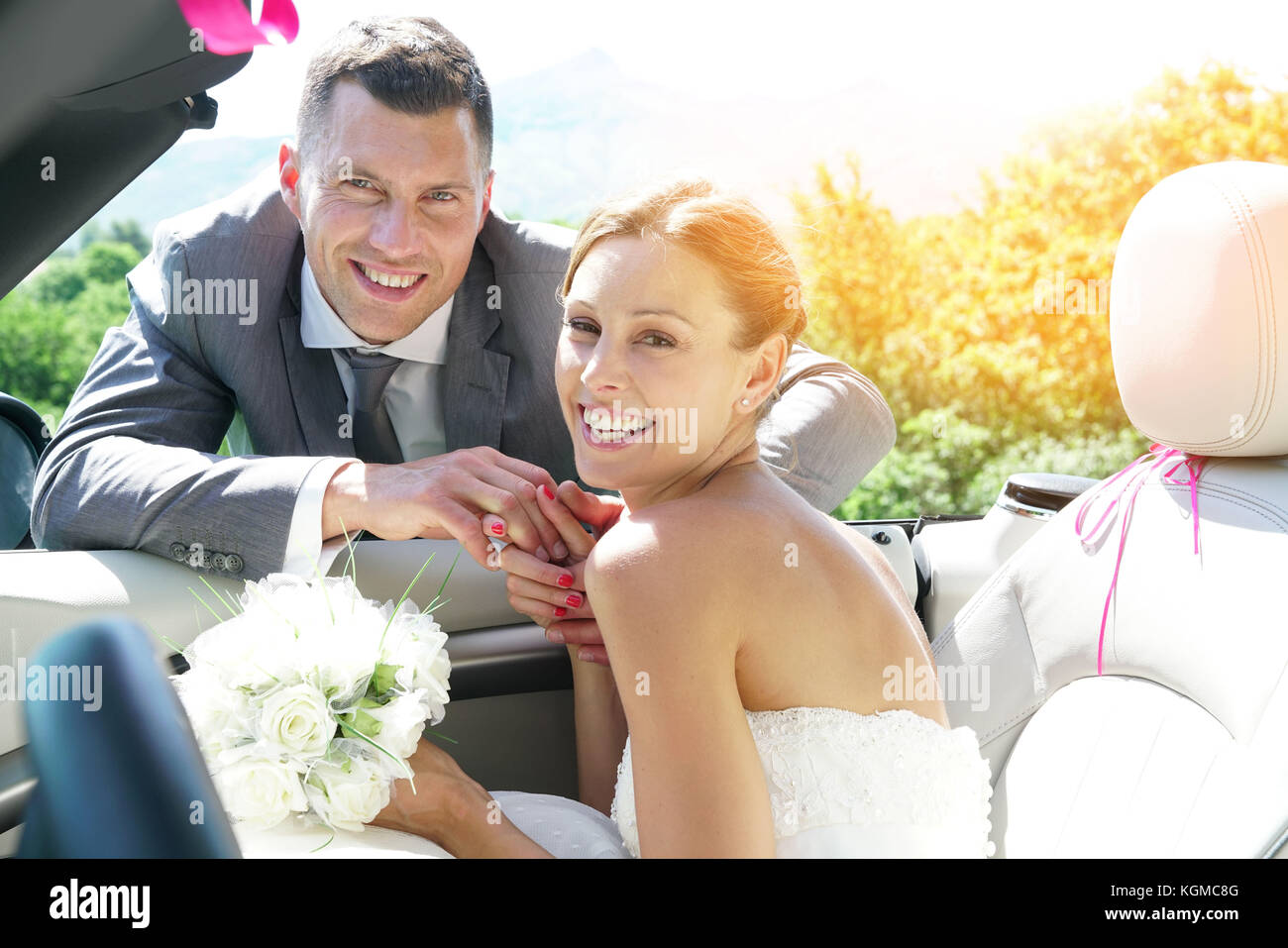Groom leading bride to get in convertible car Stock Photo - Alamy