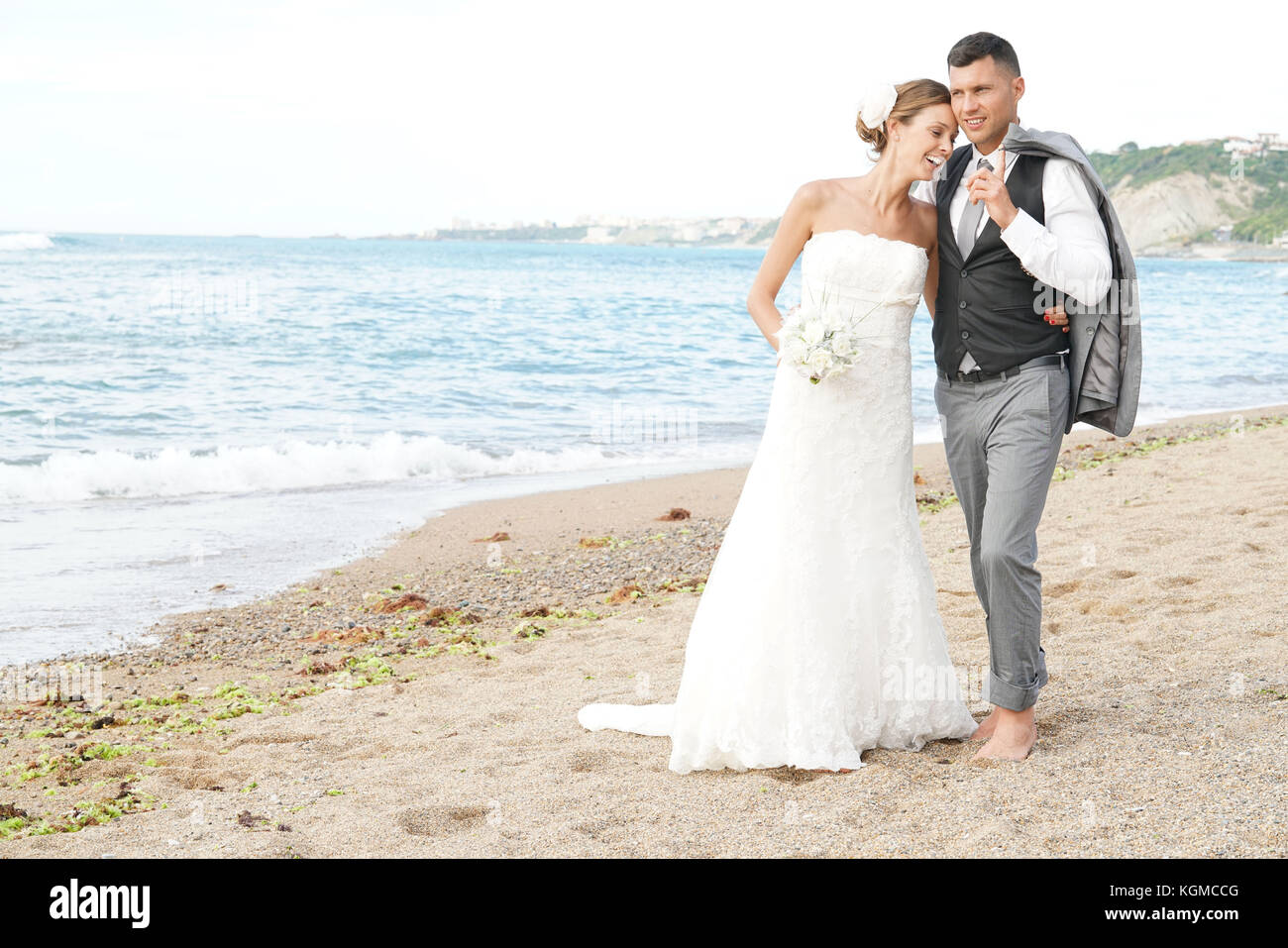 Happy bride and groom walking on beach at sunset Stock Photo - Alamy