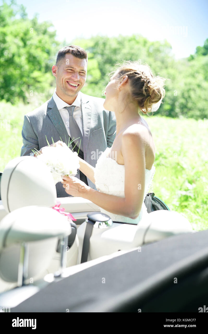 Groom leading bride to get in convertible car Stock Photo - Alamy
