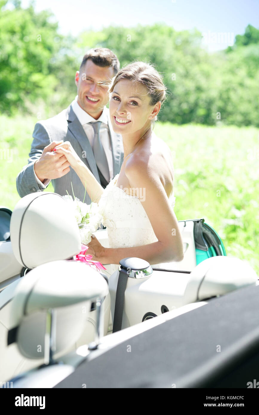 Groom leading bride to get in convertible car Stock Photo - Alamy