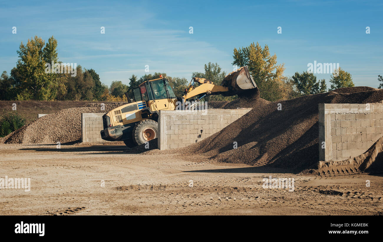 Bagger scooping gravel at construction aggregate dumps at concrete production plant Stock Photo