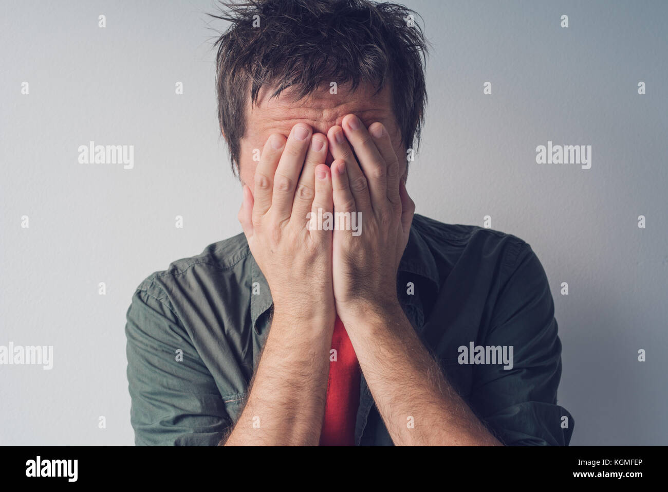 Disappointed man crying with head in hands. Sad and lonely adult male hiding tears. Stock Photo