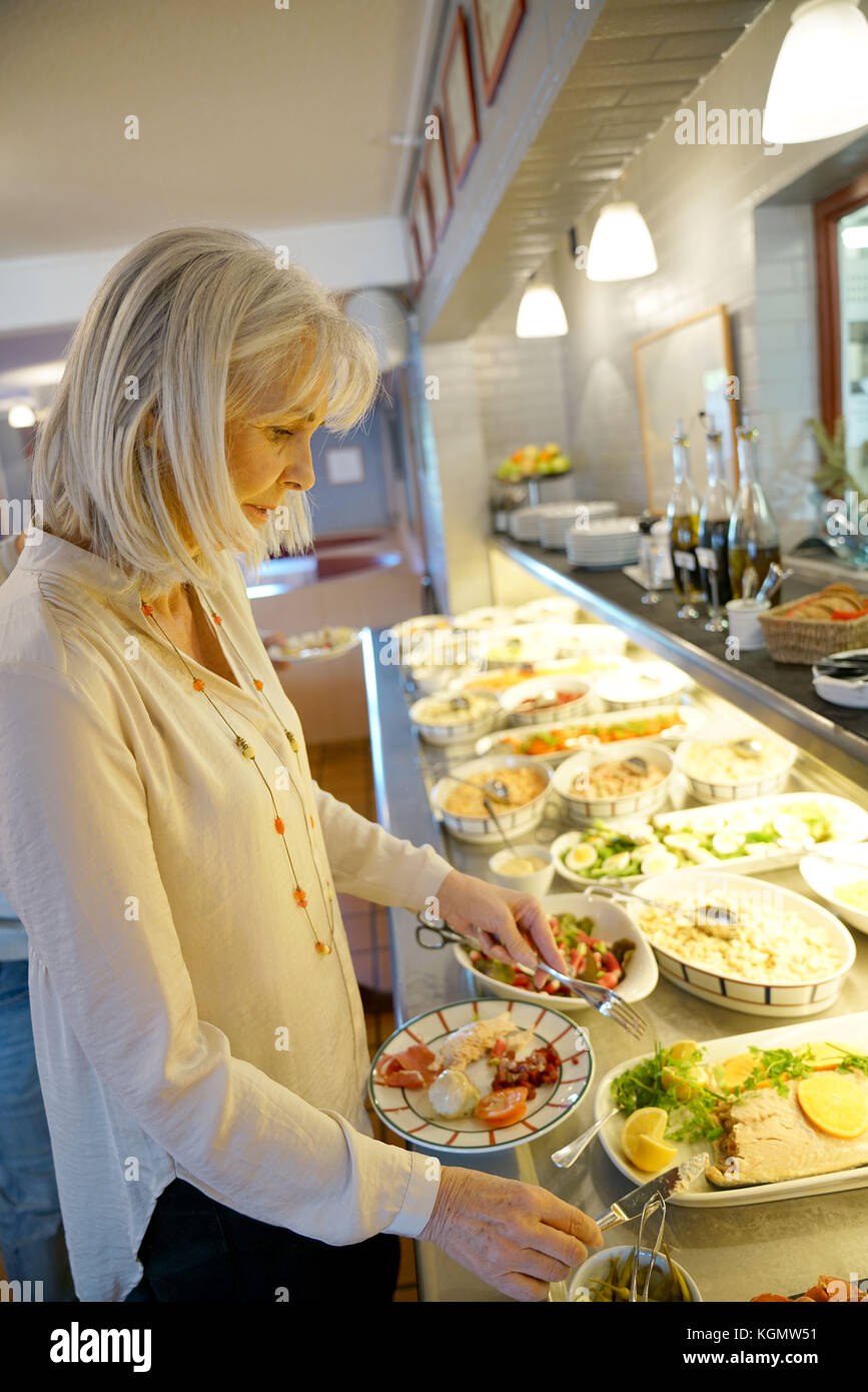 Senior woman in restaurant helping herself at delicatessen buffet Stock Photo
