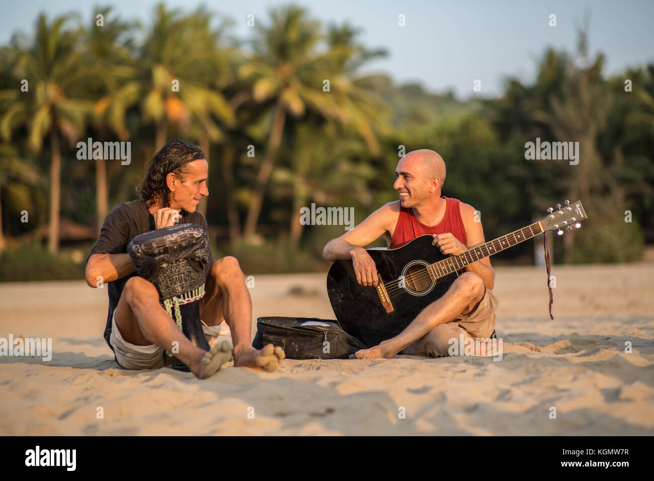 Two musicians sitting on a beach in Goa at sunset. Stock Photo