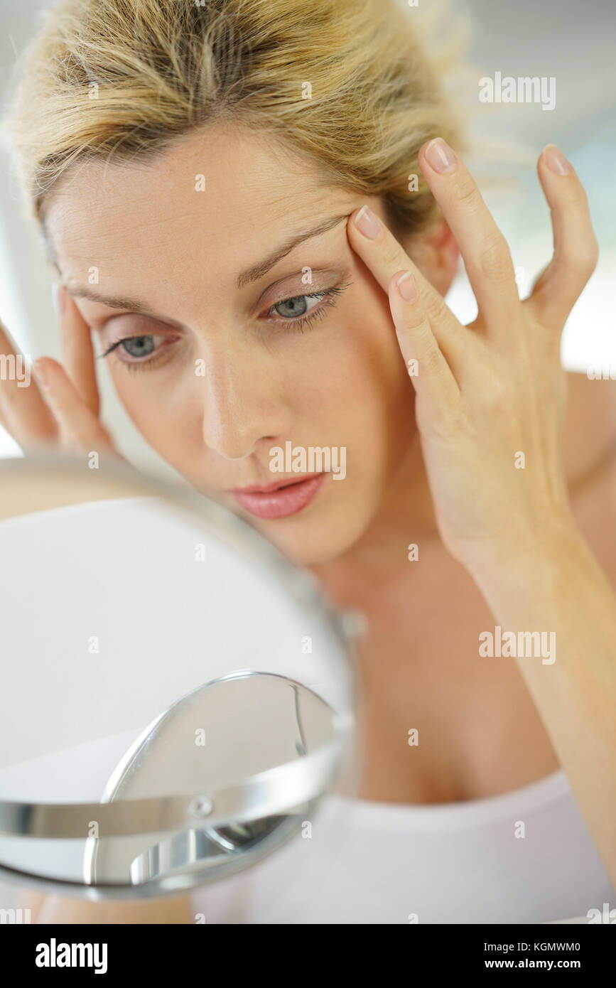 Middle-aged blond woman applying anti-aging cream in front of mirror Stock Photo