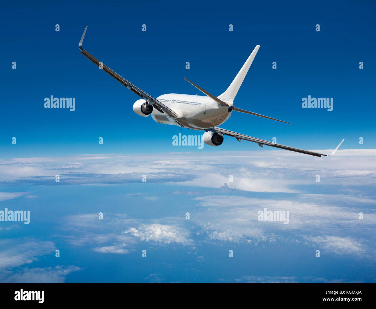 White passenger wide-body plane. Aircraft is flying in blue cloudy sky over the sea. Stock Photo