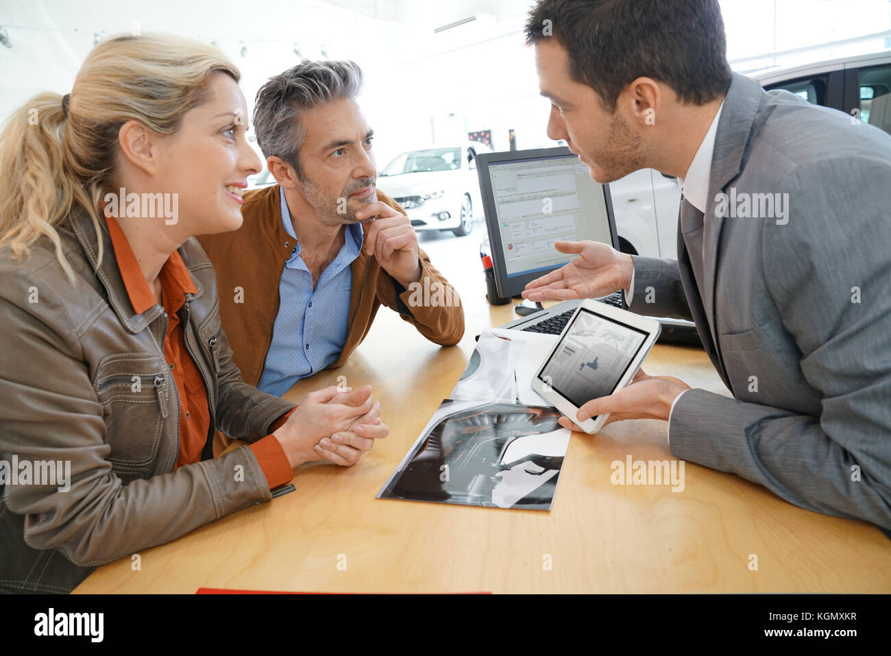Salesman in car dealership and couple looking at catalogue Stock Photo