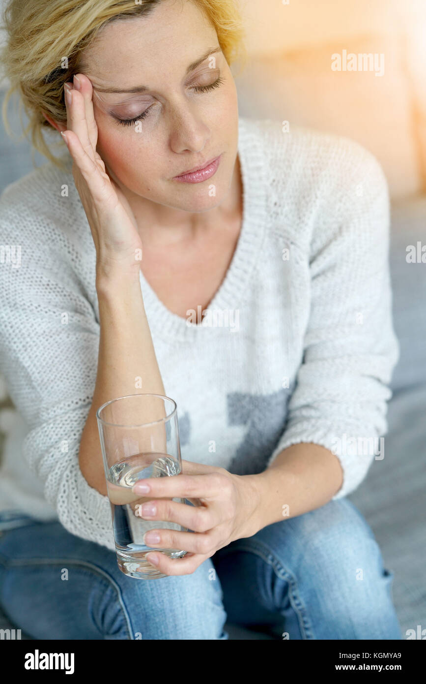 Middle-aged woman at home taking pill to ease headache Stock Photo